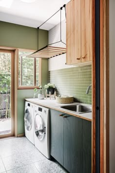 a washer and dryer in a kitchen with green tiles on the walls, wood cabinetry, and flooring