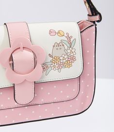 This cute handbag, in collaboration with Pusheen, features a charming pink color with white polka dots and a playful Pusheen print on the front. Made of durable leatherette, this bag also boasts an adjustable shoulder strap for comfortable carrying. The daisy belt buckle design on the front adds a touch of whimsy, while the snap button closure keeps your items secure. Inside, you'll find one zipper pocket and one slip pocket, perfect for keeping your belongings organized.Available while supplies Cute Satchel For Everyday Use, Playful Pink Shoulder Bag With Cute Design, Cute Pink Satchel Bag, Cute Pink Shoulder Bag Satchel, Cute Pink Shoulder Satchel, Cute Satchel With Removable Pouch, White Cute Satchel With Detachable Strap, Cute White Satchel With Adjustable Strap, Cute White Satchel With Detachable Strap