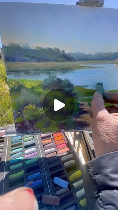 someone is painting on an easel in front of a lake with trees and grass