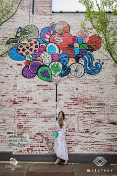 a woman standing in front of a brick wall with a tree painted on the side