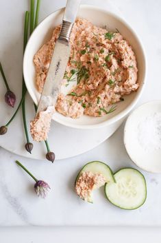 a white bowl filled with hummus and cucumbers next to sliced green onions