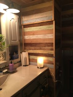 a bathroom counter with a lit candle on top of it next to a wooden wall