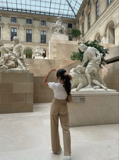 a woman standing in front of statues and looking up at the skylight above her