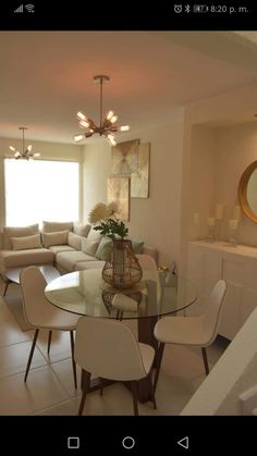 a glass table with chairs and a vase on it in front of a living room window