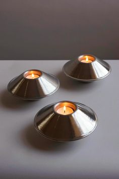 three silver candles sitting on top of a white table next to an orange lit candle