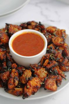 a white plate topped with fried food next to a bowl of sauce