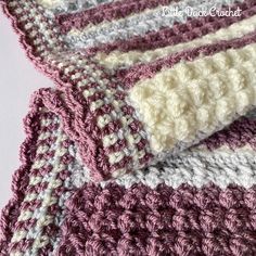 crocheted blanket laying on top of each other in shades of pink, grey and white