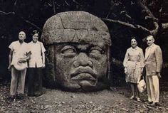 three people standing in front of a large stone statue with an angry face on it