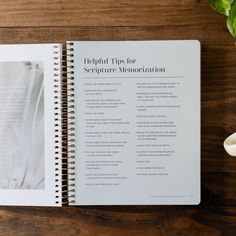 an open spiral notebook sitting on top of a wooden table next to a cup of coffee