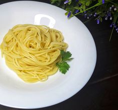 a white plate topped with pasta and parsley on top of a table next to purple flowers