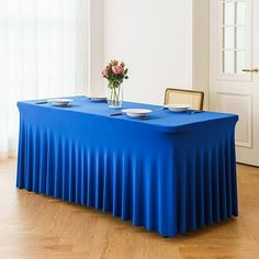 a blue table with plates on it in front of a white wall and wooden floors