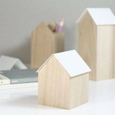 two wooden houses sitting on top of a white table next to a cell phone and pencil holder