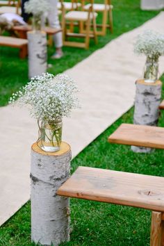 flowers are in vases placed on wooden posts at the end of a ceremony aisle