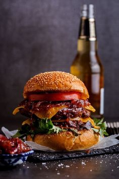 a hamburger with lettuce, tomato and cheese on it next to two beer bottles