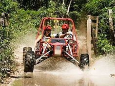 two people riding in the back of a four - wheeled vehicle through mud and trees