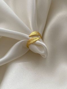 a gold ring sitting on top of a white satin material with leaves in it's center