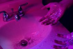 a person washing their hands in a sink with pink light from the faucet