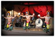 three men in hula skirts and headdress are performing on stage with drums