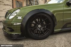 a green car with black rims parked in front of a building