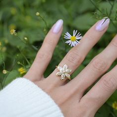 a woman's hand with a ring on it and daisies in the background