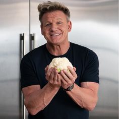 a man holding up a piece of cauliflower in front of his face and smiling