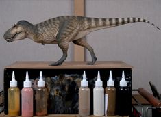 a toy dinosaur on top of a wooden box filled with paint and glue bottles in front of it