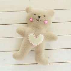 a brown teddy bear with a pink heart on it's chest sitting against a white wall