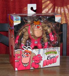 an action figure in a pink box on a wooden table next to a red curtain