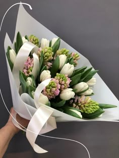 a bouquet of white tulips and other flowers is being held by someone's hand