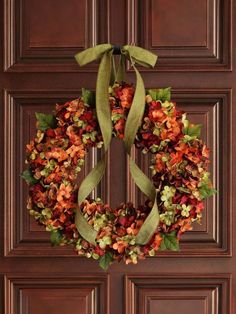 a wreath is hanging on the front door with green ribbon around it and flowers in the middle