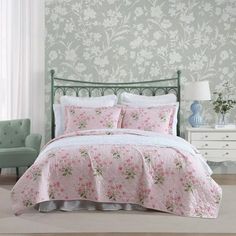 a bed with pink and white flowers on it in front of a floral wallpaper