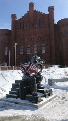 a statue of a man sitting in front of a building with snow on the ground