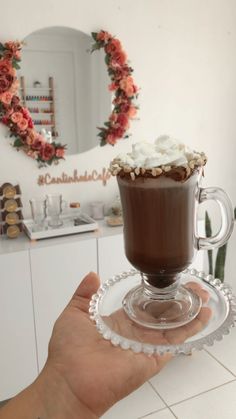 a hand holding a cup of hot chocolate with whipped cream on top in front of a mirror