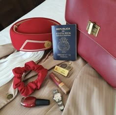 a red purse sitting on top of a bed next to a passport and other items