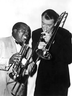 two men in suits are playing trombones and singing into each other's mouths