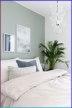 a white bed sitting under a chandelier next to a green potted plant