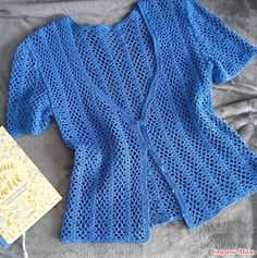 a blue knitted cardigan next to a yellow book on a gray bed sheet