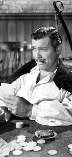 a man sitting at a table with lots of coins on the table and holding a piece of paper in his hand