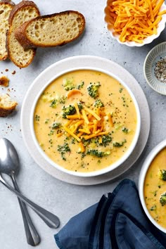 two bowls of broccoli cheese soup next to slices of bread