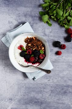 a bowl of oatmeal with berries and granola on the side next to fresh raspberries