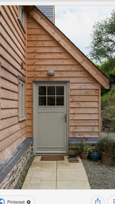 a small wooden building with a door and windows on the side of it, next to a gravel path