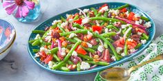 a blue bowl filled with green beans, tomatoes and feta cheese on top of a table