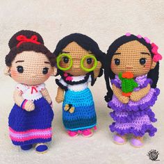 three crocheted dolls are standing next to each other on a white surface, one is wearing glasses and the other has a flower in her hand