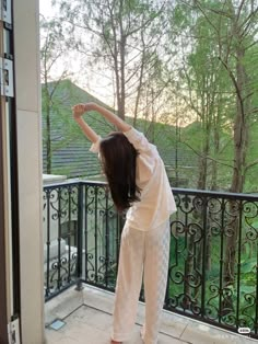 a woman is standing on the balcony with her arms in the air and looking out