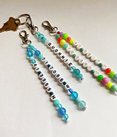 four different key chains with name charms attached to them on a white surface, one has a keychain and the other has an assortment of beads