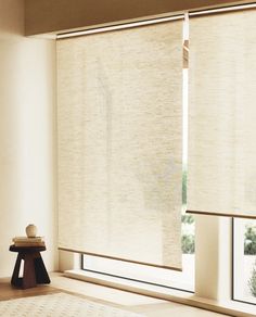 an empty room with white walls and windows covered in beige roller shades, along with a small table on the floor