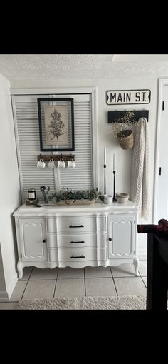 a white sink sitting under a window next to a wall with pictures and candles on it