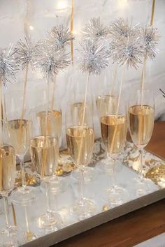 champagne flutes are lined up on a tray with sparklers in the middle and small silver balls sticking out of them