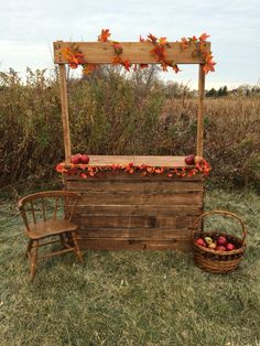 an outdoor fruit stand with apples and flowers on the top, next to a wooden chair