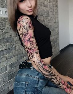 a woman with a tattoo on her arm posing for the camera in front of a brick wall